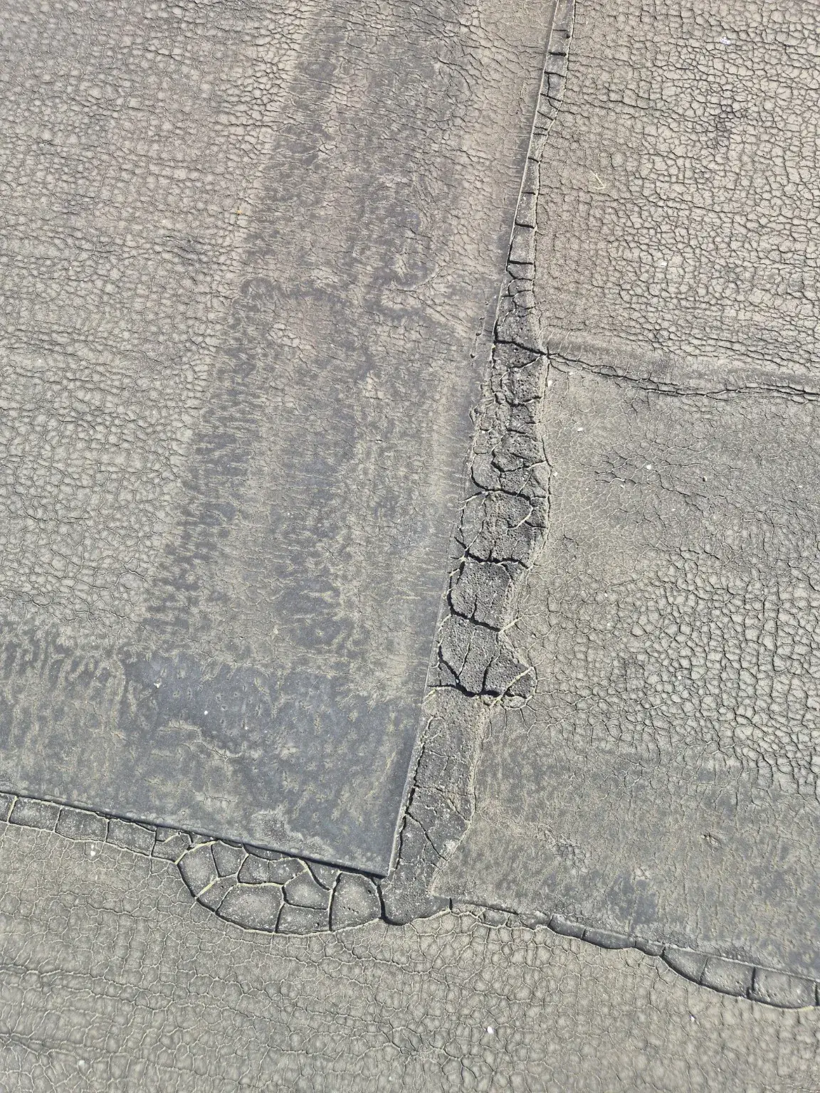 Verouderde bitumen dakbedekking met craquelé en een beschadigde naad