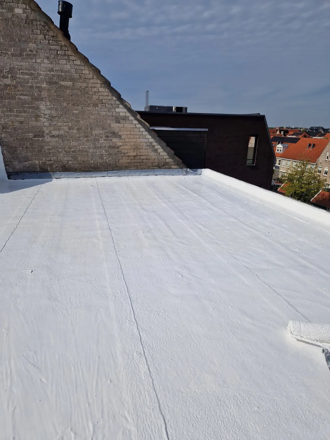Wit eindresultaat langs de gevel bij bitumendak in hellevoetsluis met siliconen dakcoating